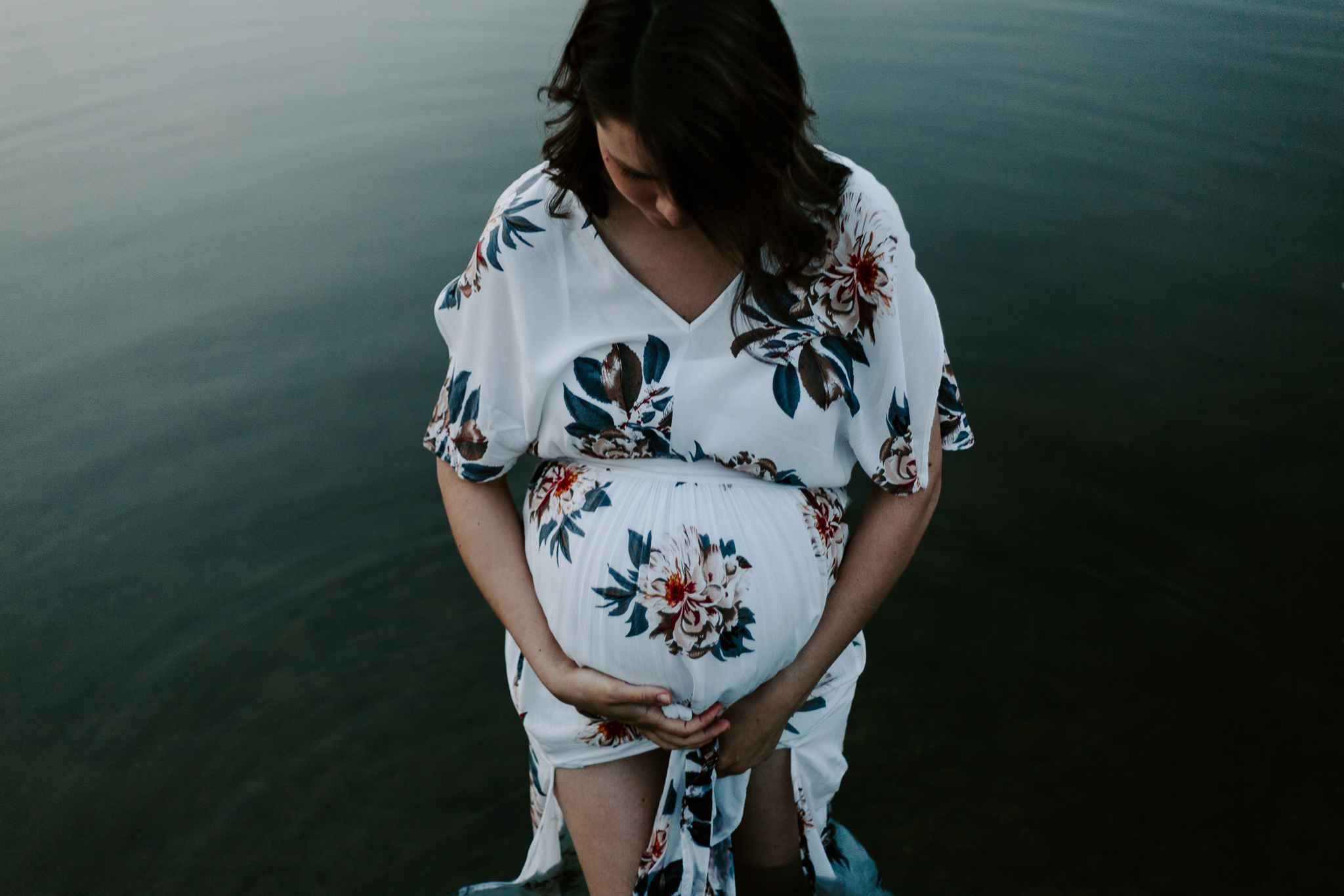 Pregnant mother in a floral maxi dress wading in pond at blue hour.